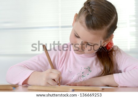 young pretty girl in a pink sweater drawing at the table at home