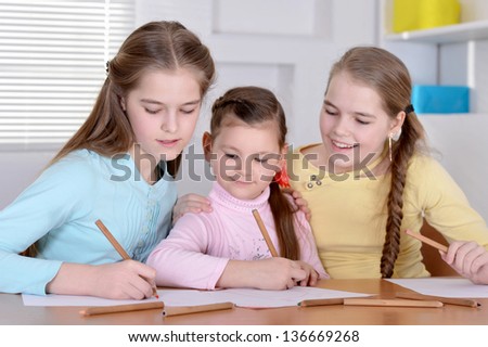 three young girls  draw with pencils  at the table at home