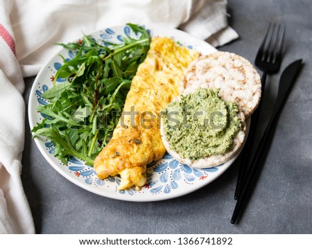Healthy breakfast - scrambled eggs, arugula and bread with pesto on gray background. Perfect eggs omelette with fresh arugula and pesto cracker. Vegetarian food. Diet. Selective focus, close up