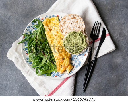 Healthy breakfast - scrambled eggs, arugula, bread with pesto on gray background. Perfect eggs omelette with fresh arugula and pesto cracker. Vegetarian food. Diet. Selective focus, close up, top view