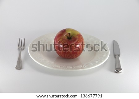 Red and yellow apple on white dish with fork and knife