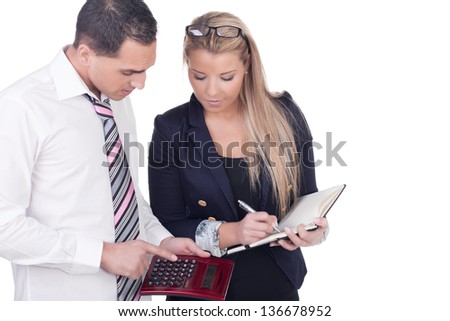 Work colleagues comparing figures with the man analysing the statistics on a calculator while the woman looks on waiting to write the information in a notebook, upper body studio portrait on white