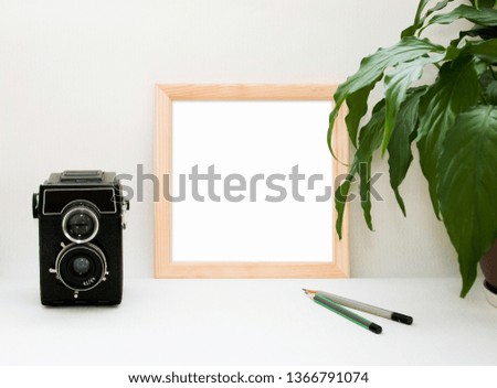Mock up wooden frame, old camera, plant and pencils. Interior home square poster mockup with wood frame and green leaves on white wall background. Retro template for poster, picture, art painting.