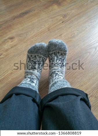 Women's legs with rolled-up pants in warm wool socks white with black pattern, standing on the wooden floor Royalty-Free Stock Photo #1366808819