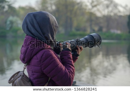 a young girl wearing hijab ready to take a picture with her camera and tele lens.