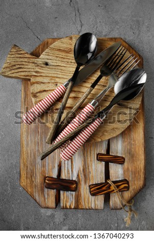 Cutlery on gray concrete background. Spoon, fork, knife with white and red stripes on handles on wooden serving board