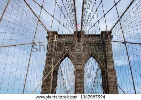 The famous Brooklyn Bridge Bridge located in New York City in the United States of America showing the suspension wired and the USA flag at the top of the column on a part cloudy day with blue Skys.