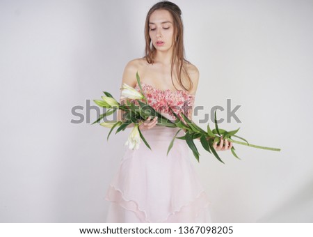charming young caucasian girl in a pink long dress holds a lush Lily flower in her hands and stands on a white background in the Studio