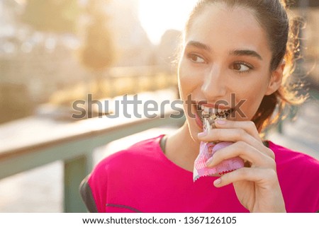 Athletic woman eating a protein bar. Closeup face of young sporty woman resting while biting a nutritive bar. Fitness beautiful woman eating a energy snack outdoor. Royalty-Free Stock Photo #1367126105