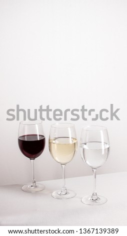 Three glasses of red, white wine and water standing in one line on grey background. vertical picture with copy space