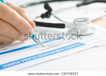 Doctor completing a Medical Insurance Claim Form by Stethoscope 
