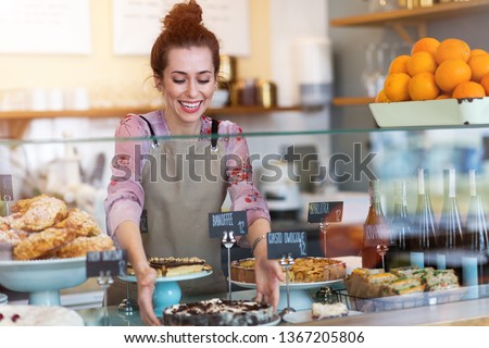 Woman working in coffee shop in Warsaw, Poland. Translation on black cards: „Banoffee Pie", „Fruit Cake”, „Apple Pie”, „Sandwiches”