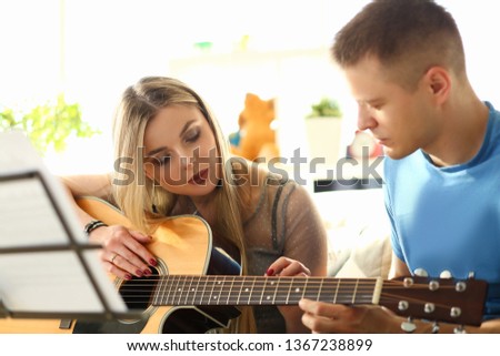 Millenial woman and guitar teacher play music sitting sofa home room background.