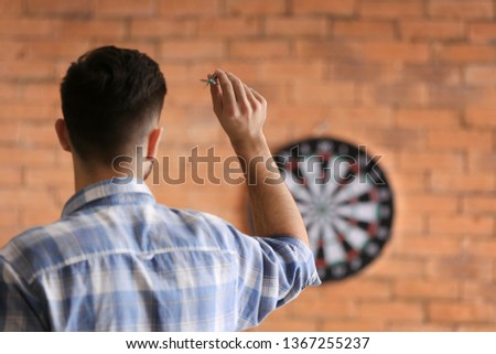 Young man playing darts indoors Royalty-Free Stock Photo #1367255237