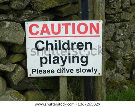 'Caution: children playing' sign against dry stone wall in Cumbria, England