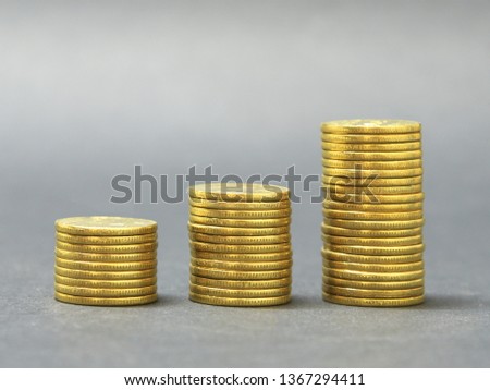 Three stacks of golden coins in ascending order against grey background. Grooved edge of coins. Growth of economy, concept. Financial growth.