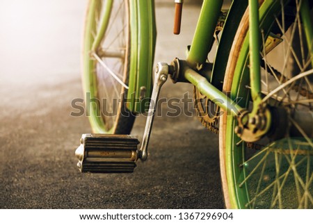  The pedal and wheels of an old vintage green Bicycle, which stands on the asphalt and is illuminated by the sun.