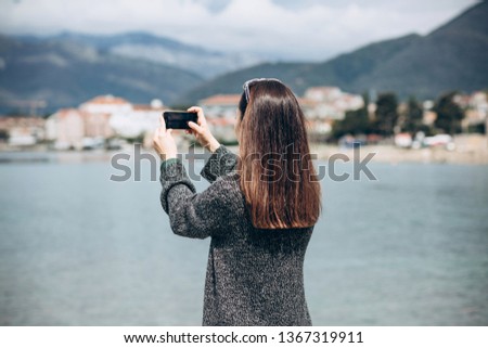 A girl or a tourist photographs a beautiful view of the sea and the urban architecture of the small coastal town of Tivat in Montenegro.