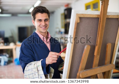 Creative male artist drawing picture with oil paints in studio