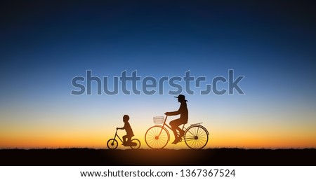 Widescreen Silhouette mother and son riding bicycle on hill under sunset sky background