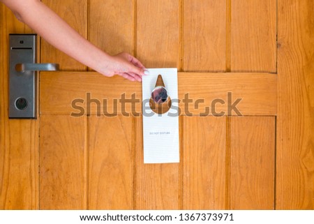 Woman hand holding and hangs signboard do not disturb on the door in hotel.