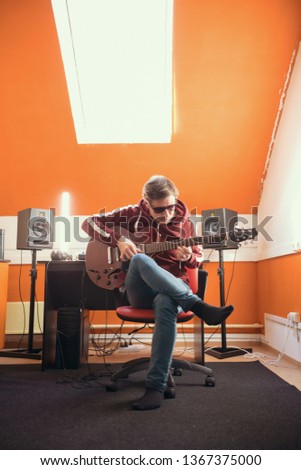 A man in glasses working in the studio. Playing guitar