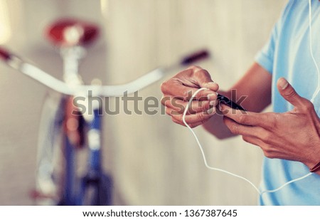 people, technology and lifestyle - close up of young hipster man with earphones, smartphone and bicycle listening to music