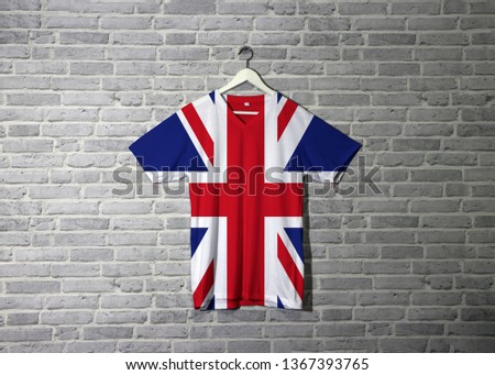 Union jack flag on shirt and hanging on the wall with brick pattern wallpaper. Cross of Saint Andrew counterchanged with the Cross of Saint Patrick, over all the Cross of Saint George.