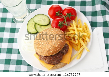Beef Cheese Hamburger with french fries, lettuce, tomato, onion, cucumber, ketchup and mayonnaise on wooden table.