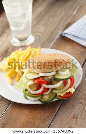Vegetarian "Burger" Sandwich with french fries, tomato, cucumber, onion, lettuce, paprika on wooden table