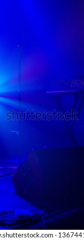 Keyboard on empty stage with blue ambient stage lights. Synthesizer and stage speaker.