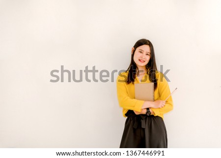 The girl standing holding writing in a notepad while standing on a white background