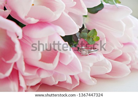 Macro shot of expensive white gold diamond ring and beautiful tender pink tulips. Top view composition with engagement ring and flower petals. Feminine wedding background with copy space for text.
