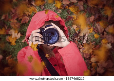 Woman focusing a camera laying in autumn leaves