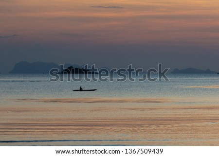 Fisherman in the kayak on the ocean in sunset sky.Silhouettes of human is paddling on kayak at sea with city views when sunset. Silhouette of a man kayaking in the open sea at sunset.