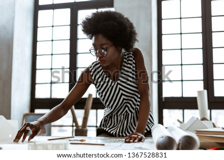 Striped blouse. African-American interior designer wearing striped blouse working hard in the office Royalty-Free Stock Photo #1367528831