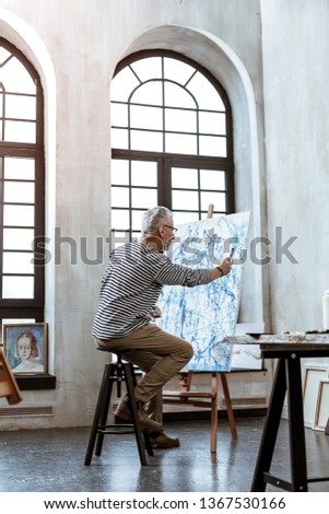 Spacious workroom. Grey-haired artist feeling excited while painting on canvas in spacious workroom
