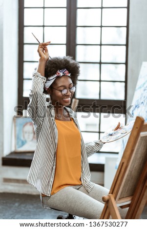 Cheerful and happy. Beautiful African-American artist feeling cheerful and happy while painting all day