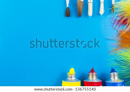 water colors, paint brushes and feathers on blue background