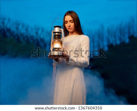 Mysterious mystical girl in a dark night forest with a kerosene lamp in her hands Halloween concept