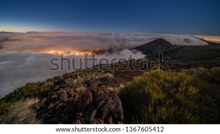 Teide National Park, Above the clouds with a view in a valley with a illuminated city at Night.
