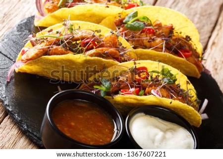 Delicious tacos stuffed with glazed chicken, microgreen and vegetables served with sauces close-up on a slate board on the table. horizontal
