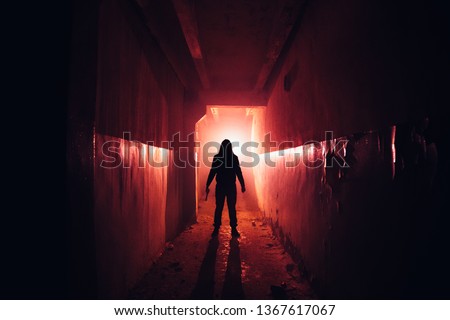 Creepy silhouette with knife in the dark red illuminated abandoned building. Horror about maniac concept. Royalty-Free Stock Photo #1367617067