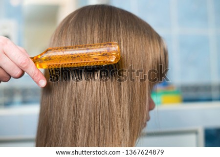 Mother hand with brush combing long fair hair of cute child girl after bath on blurred interior background.