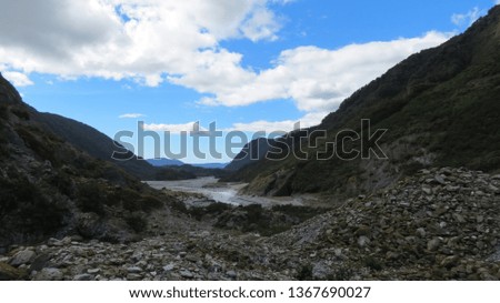 Rocky foreground with mountains and a river bed snaking away. A moody landscape with a crisp blue sky and lingering clouds in New Zealand.