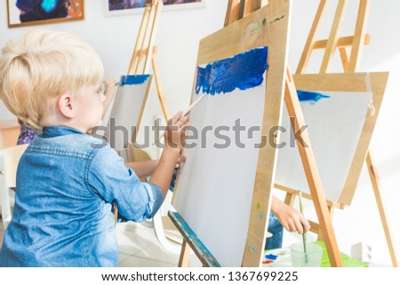 little boy with a teacher in group of preschool student sat the drawing a picture. Painting on maelbert, palette and paints. Back to school and Education concept