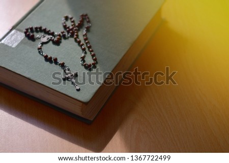 Detail of a silver small crucifix with rosary beads and old book of Catholic Church on a wooden table 
Beautiful background.Religion concept.