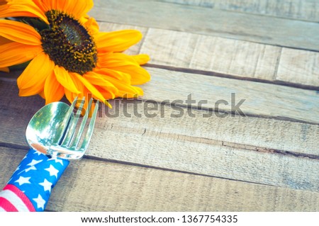 Fourth of July Picnic or BBQ Table Place Setting with Red, White, and Blue, stars and stripes napkin around fork and knife with sunflower on Rustic Wood Board background.  Cross Processing  for mood