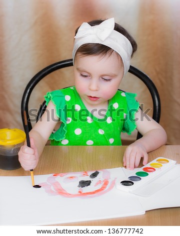 Little girl draws paints sitting at the table.