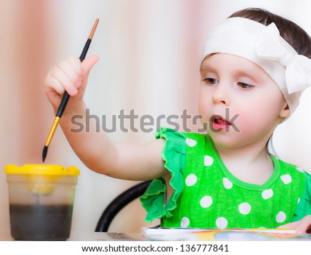 Little girl draws paints sitting at the table.